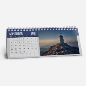 September 2027 desk calendar with mountain landscape and lighthouse photo.